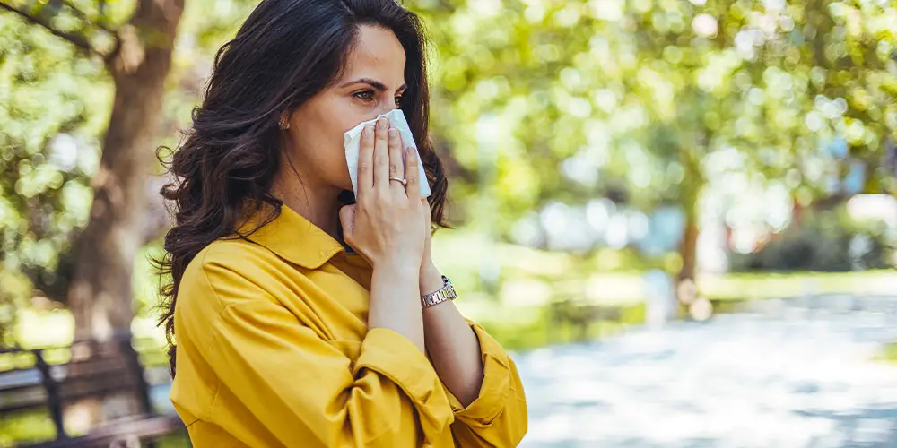 A woman in a public park suffering from hay fever, seasonal allergies.